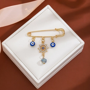 Macro detail of gold evil eye brooch with nautical helm and blue teardrop pendant in gift box