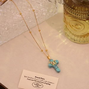 Detail of turquoise cross pendant on a gold chain with butterfly accent and vintage props