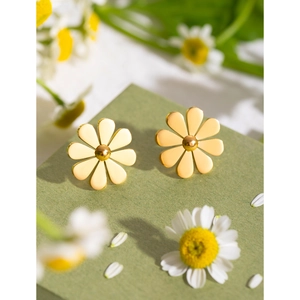 Macro detail of 18k gold plated daisy stud earrings on dark green textured surface