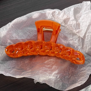 Close-up of vibrant orange chain-link claw clip with transparent acrylic texture