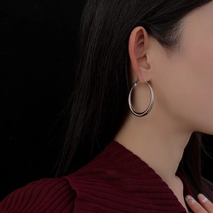 Close-up of minimalist silver hoop earring worn by a model against a dark background