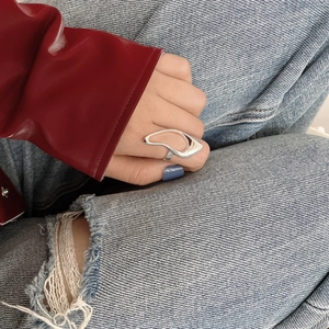 Close-up of irregular wavy S925 sterling silver ring worn on hand with blue denim jeans