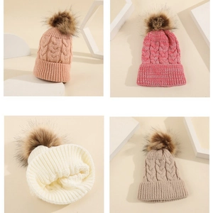 Close-up of cable knit beanie hats in pink, red, white and khaki with fluffy fur pom poms