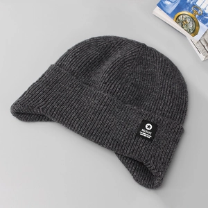 Flat lay of a thick dark gray knit winter beanie with ear flaps and branded woven tag
