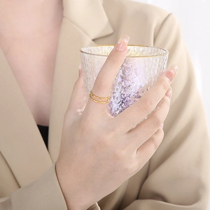 Detail of double-layered wave ring in gold finish worn by model holding glass