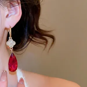 Elegant gold drop earrings with diamond clover and red pear-shaped pendant on model
