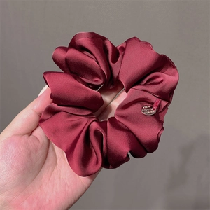 Deep red satin scrunchie with silk luster and a small round metal tag detail