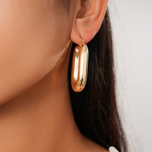 Close-up of a large gold oval hoop earring with polished finish on a model's ear