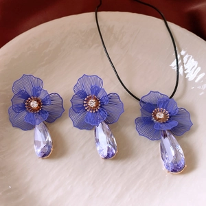 Détail d'une parure florale avec pétales bleus et pendentifs en cristal violet sur plateau