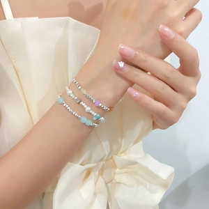 Close-up of three layered silver-beaded bracelets with pastel pearls on a model's wrist