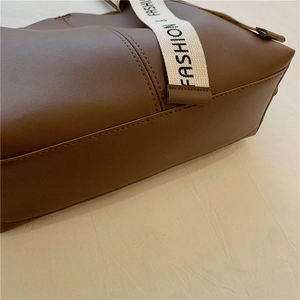 Large brown tote bag with detailed stitching and cream-colored fashion logo strap