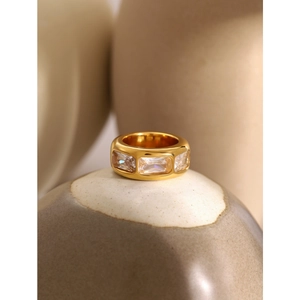 Macro shot of gold wide band ring with three rectangular zircons on ceramic tray