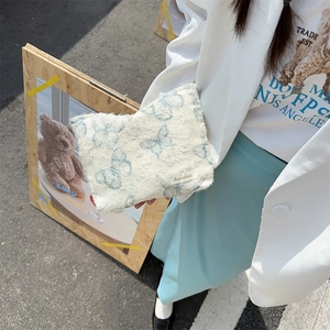 Close-up of a white plush makeup bag featuring blue butterfly embroidery and woven label