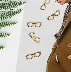 Flat lay of gold eyewear charms for DIY jewelry making with green fern accents