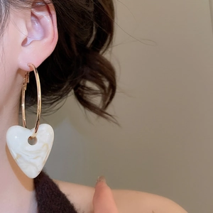 Close-up of golden hoop earring with large white marble acrylic heart pendant