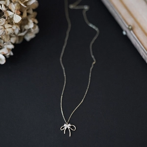 Detail of a golden S925 sterling silver necklace featuring a double-layered bow pendant