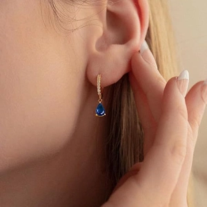Close-up of gold hoop earrings with sparkling zircon and a blue teardrop stone