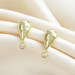 Primer plano de pendientes de gota chapados en oro con circonitas en tela