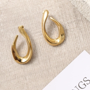 Close-up of golden irregular twisted oval stud earrings on textured beige fabric