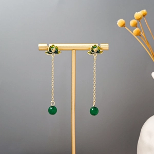 Detail of long tassel earrings with green lotus enamel and beads on a gold stand