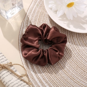 Detailed texture of coffee brown silk satin scrunchie on a decorative woven mat