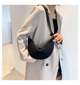 Detail of black corduroy dumpling bag with adjustable strap worn on a beige blazer
