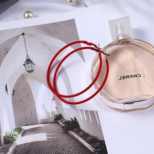 Détail de grandes créoles rouges mates posées à côté d'un flacon de parfum de luxe