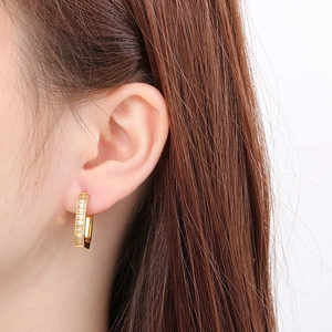 Close-up of gold U-shaped earrings with rectangular zircons worn by a female model