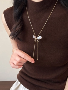 Detail of gold butterfly necklace with iridescent shell wings and tassel on a sweater