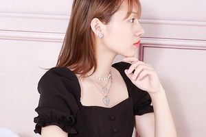 Close-up of layered silver pearl necklace and heart earrings on model with soft lighting