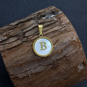 Gold round pendant with natural shell inlay and letter B on a rustic wood background