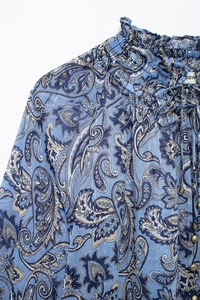 Dettaglio di camicetta in chiffon paisley blu con colletto in pizzo e bottoni dorati