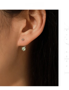 Close-up of a silver six-prong earring with a round light green moissanite on an ear
