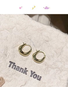 Macro shot of 18K gold plated U-shaped hoop earrings on textured beige paper