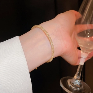 Détail d'un bracelet doré à texture grillagée au poignet avec un verre de vin