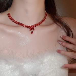 Close-up of golden necklace with leaf-shaped red gemstones and a teardrop pendant