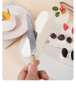 Close-up of a serrated stainless steel knife with wooden handle cutting a cream cake