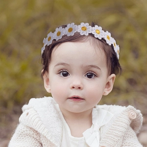 Close-up of a baby wearing a white daisy elastic headband in a soft natural outdoor setting