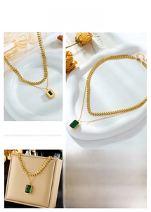 Detail of layered gold chain necklace featuring an emerald-cut green gemstone pendant