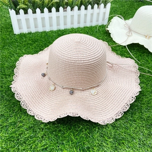 Détail de chapeau de soleil en paille rose avec dentelle et breloques en nacre