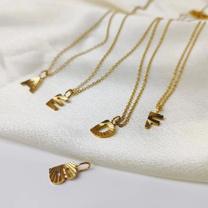 Detailed macro view of gold letter pendants with radial texture on white silk background