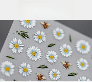 Macro detail of 5D daisy and bee nail art stickers with embossed texture and green leaves