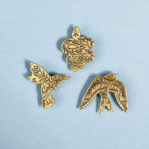 Vue détaillée de broches vintage en métal doré avec gravures de colibri et d'hirondelle