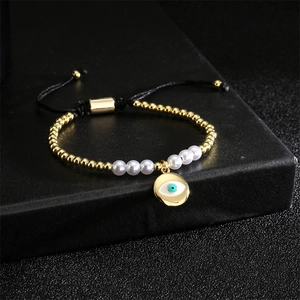 Detail of evil eye pendant with gold beads and white pearls on adjustable woven bracelet