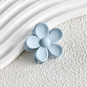 Macro detail of a light blue matte flower hair claw clip on a white stone background