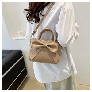Close-up of a beige bow-knot crossbody bag with adjustable strap on a model