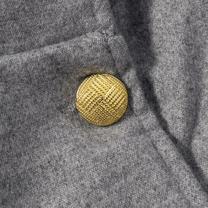 Detailed close-up of a gold metal button on high-quality grey wool blend fabric texture