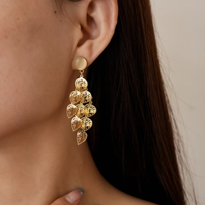 Close-up of gold hollow leaf tassel earrings with cat eye stones worn by a model