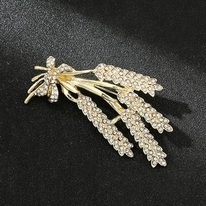 Macro shot of gold wheat ear brooch encrusted with sparkling white rhinestones on black background