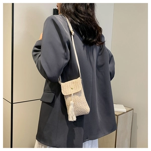 Dettaglio borsa porta cellulare in paglia intrecciata con nappa beige e patta di chiusura